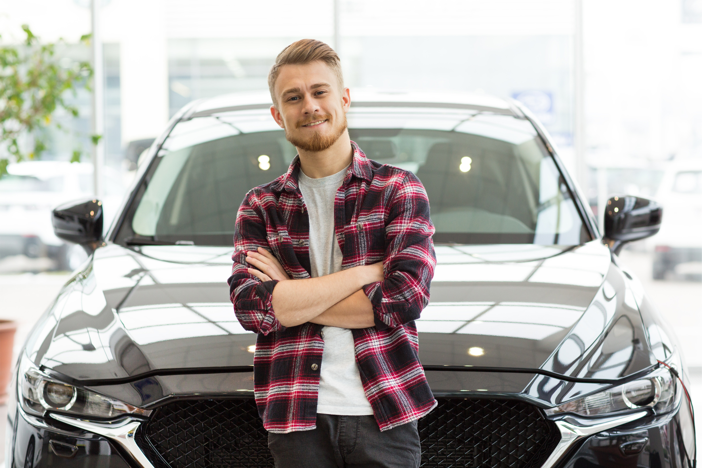 A happy young man is standing in front of his car after an auto loan refinance.